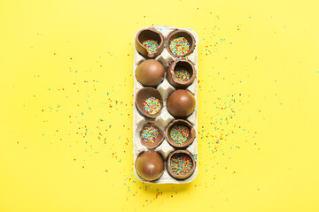 Holder with delicious chocolate eggs with sprinkle fillings on yellow background