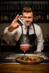 Selective focus on glass with pink foamy cocktail which hand of male bartender sprinkles it with sugar powder.