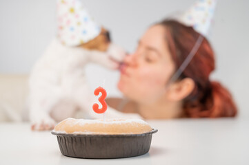 Caucasian woman and jack russell terrier in holiday caps look at the cake with a candle. The dog...
