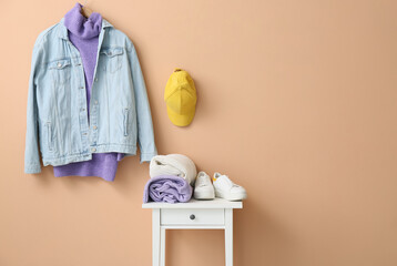 Stylish clothes and shoes on table near color wall