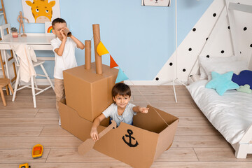Funny little boys playing with cardboard ship at home