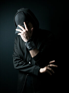 Man standing alone in the dark wearing a black hoodie and hat