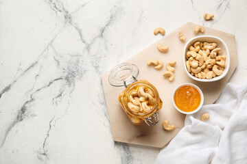 Fototapeta na wymiar Jar of tasty cashew nuts with honey on white marble background