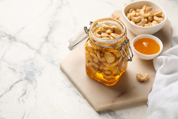 Jar of tasty cashew nuts with honey on white marble background