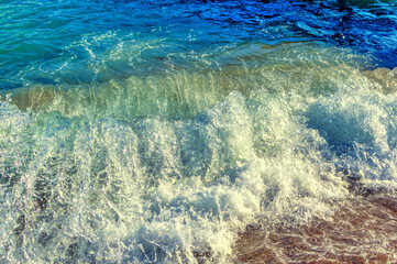 Sea wave splashing sandy beach during summer day.