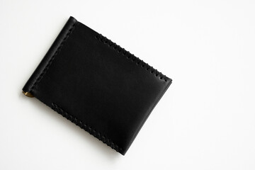 Empty black men's money clip handmade leather wallet with a two pockets for cards lies on a white table. Selective focus, copy space, close up.
