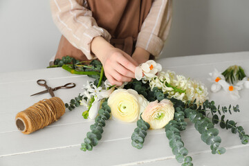 Female florist making bouquet of beautiful flowers at white wooden table - obrazy, fototapety, plakaty