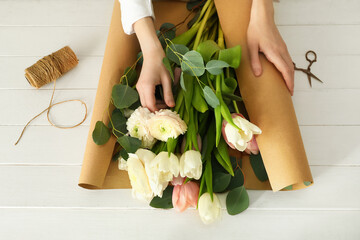 Female florist wrapping in craft paper beautiful bouquet at light wooden background - obrazy, fototapety, plakaty