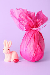 Chocolate Easter egg wrapped in paper and bunny on lilac background