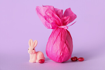 Chocolate Easter egg wrapped in paper and bunny on lilac background