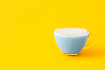 Glass cup of blue matcha tea on yellow background