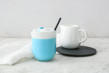Glass of blue matcha tea and jug with milk on light background
