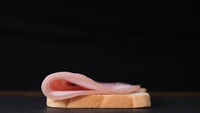 Preparation of sandwich with ham. Chef is cooking sandwich with prosciutto cotto, male hands takes a slice of prosciutto and puts it on a white bread, making of fast food with boiled pork, close-up