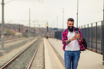 Portrait of young caucasian man using mobile phone at train station.