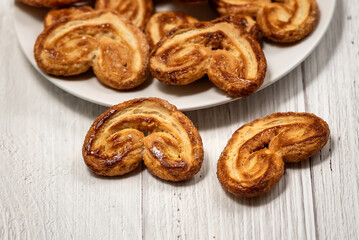 Palmier puff pastry biscuits in white plate on a white painted wooden table