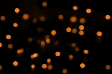 Defocused bokeh lights on black background, an abstract naturally blurred backdrop for Christmas eve or birthday party. Festive light texture. Yellow and red garland in blur. Overlay effect for design