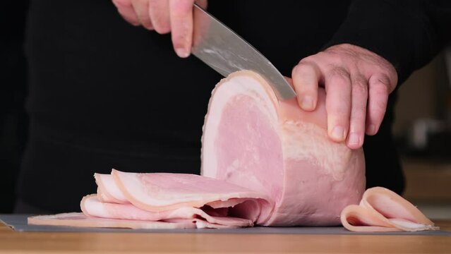 Prosciutto cotto with lard. Slicing traditional ham into pieces on cutting board with a knife. Thin slices of meat. Concept of delicious food snacks and cooking. Man with knife is cutting slim slices 