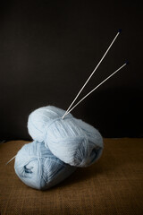 Image of some balls of blue yarn with knitting needles on dark background and copy space