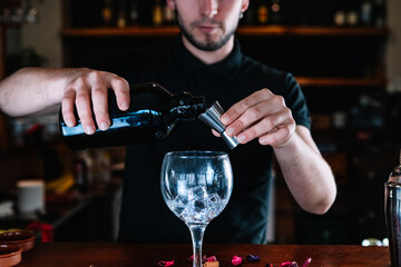 Detail of the hands of a bartender using a liquid meter for the making of a mixed drink, on the bar counter.