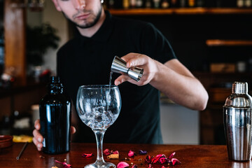 waiter pouring liquor into a glass cup to prepare a mixed drink on the bar counter.