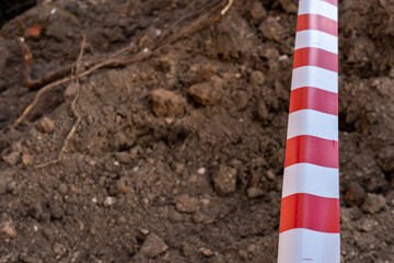 Red and white barrier tape protect a danger place. The warning tape indicates the danger of being on the territory of the construction site. Dug trenches for laying new pipes.