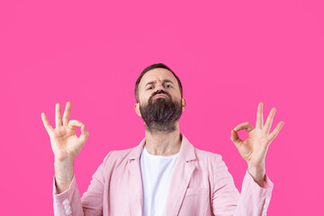 Naklejka premium Portrait of a smiling young man in a pink jacket. Man showing ok gesture while standing in studio over isolated red background.