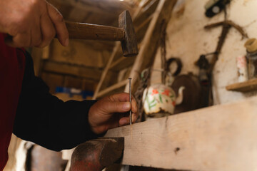 An old man in his workshop working on wood with hammer and handsaw 