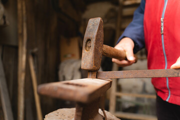 An old man in his workshop working on wood with hammer and handsaw 