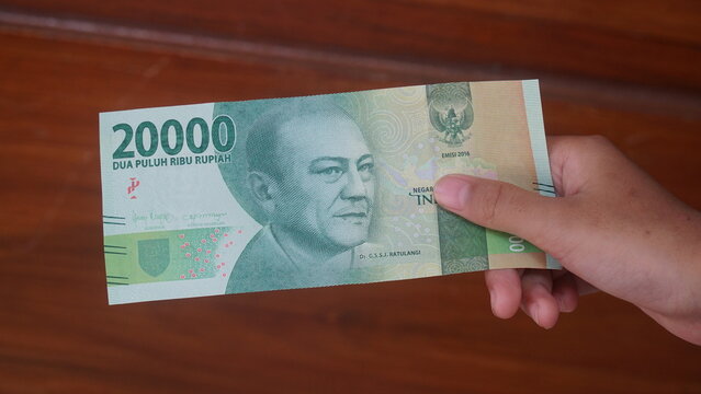 The Indonesian currency, the 20,000 rupiah note, is held in a woman's hand