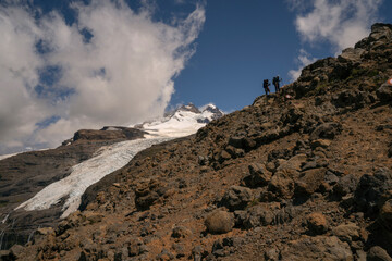 Alpine scenic. View of two hikers climbing up Tronador hill and glacier Castaño Overo in the Andes mountains in Patagonia Argentina. The rocky mountaintop and glacier ice field in a sunny day. 
