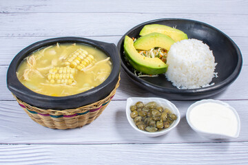 Ajiaco, traditional Colombian food, accompanied by rice, milk cream, avocado, capers and salad