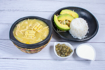 Ajiaco, traditional Colombian food, accompanied by rice, milk cream, avocado, capers and salad