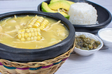 Ajiaco, traditional Colombian food, accompanied by rice, milk cream, avocado, capers and salad