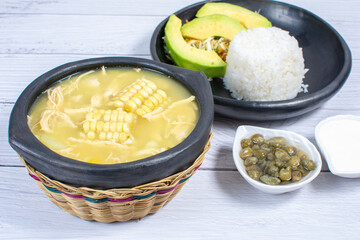 Ajiaco, traditional Colombian food, accompanied by rice, milk cream, avocado, capers and salad