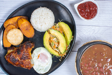 Traditional Colombian lunch, accompanied by chicken, beans, fried egg, arepa, rice, avocado, ripe plantain and salad
