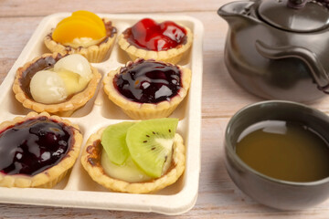 Homemade Fruits tarts, Sweet desserts topping with fresh kiwi, blueberries, peach, longan, raspberries in syrup, served with hot herbal tea on wooden table	
