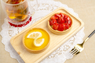 Fresh baked Lemon Tart topping with lemon sliced and Fresh Strawberries Tart topping with strawberries sliced, serving on wooden plate with hot tea, good for sweet teatime