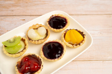 Homemade Fruits tarts, Sweet desserts topping with fresh kiwi, blueberries, peach, longan, raspberries in syrup, on wooden table	
