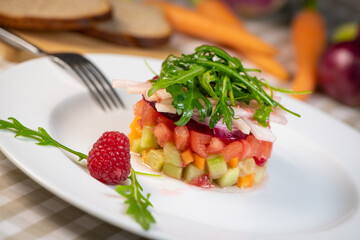 Tartare of fresh diced vegetables and salads in a white plate decorated with a raspberry