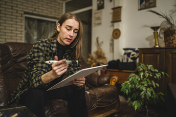 One young beautiful caucasian woman artist sitting on the bed sofa at home painting on the canvas holding paintbrush art and creativity professional or hobby concept real people side view copy space