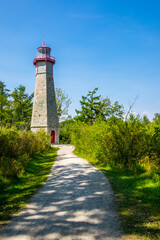 A partially shaded path leads to the old stone Gibraltar Point lighthouse bathed in sunlight.