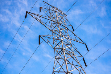 Looking up at a steel hydro tower and power lines against a blue sky.