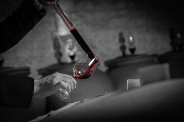 FRANCE, GIRONDE, SAINT-EMILION, SAMPLING A GLASS OF WINE IN A BARREL WITH A PIPETTE FOR TASTING AND...