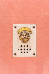 Golden lion anonymous door bell on a peach plaster wall, Venice Italy