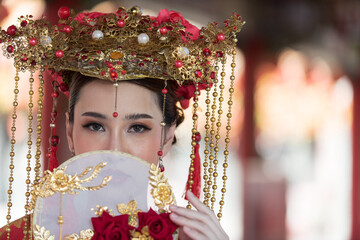 Obraz premium chinese new year celebration. portrait of a woman. Beautiful young woman in a bright red dress and a crown of Chinese Queen posing against the ancient door. Chinese Letter meaning about the happiness 
