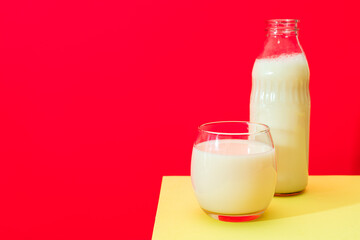 Glass bottle and big glass with milk on yellow table with red background.