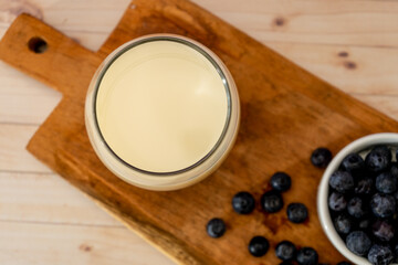 Top view of a glass of milk next to some blueberries on a wooden board on a table. Healthy eating