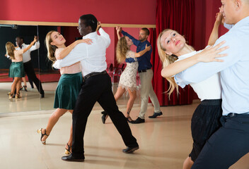 Adult dancing couples enjoying foxtrot in dance studio..