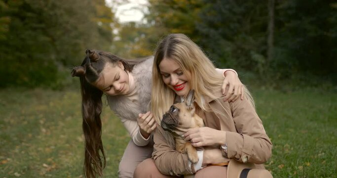 Joyful mother and daughter playing with dog in a par