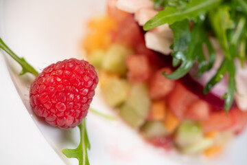 Tartare of fresh diced vegetables and salads in a white plate decorated with a raspberry